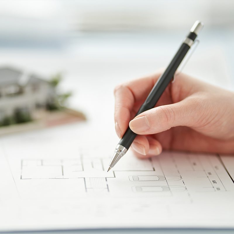 図面に鉛筆で書き込む手と住宅模型